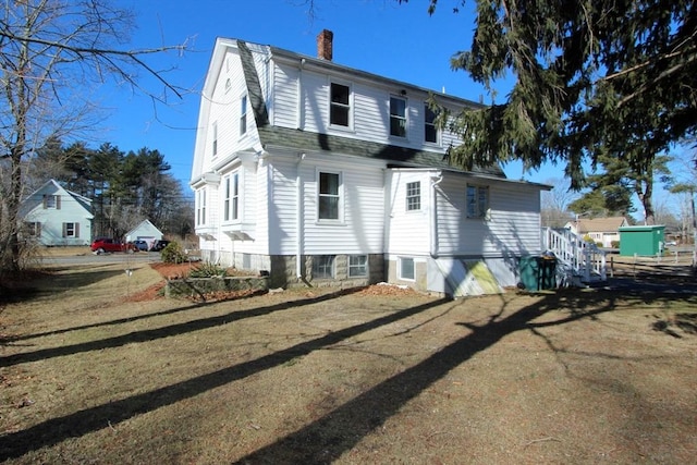 rear view of property with a shingled roof, a yard, a chimney, and a gambrel roof