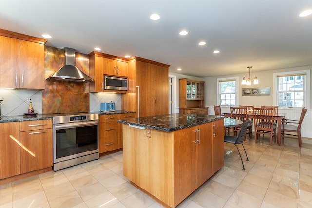 kitchen featuring a notable chandelier, stainless steel appliances, decorative light fixtures, a kitchen island, and wall chimney exhaust hood