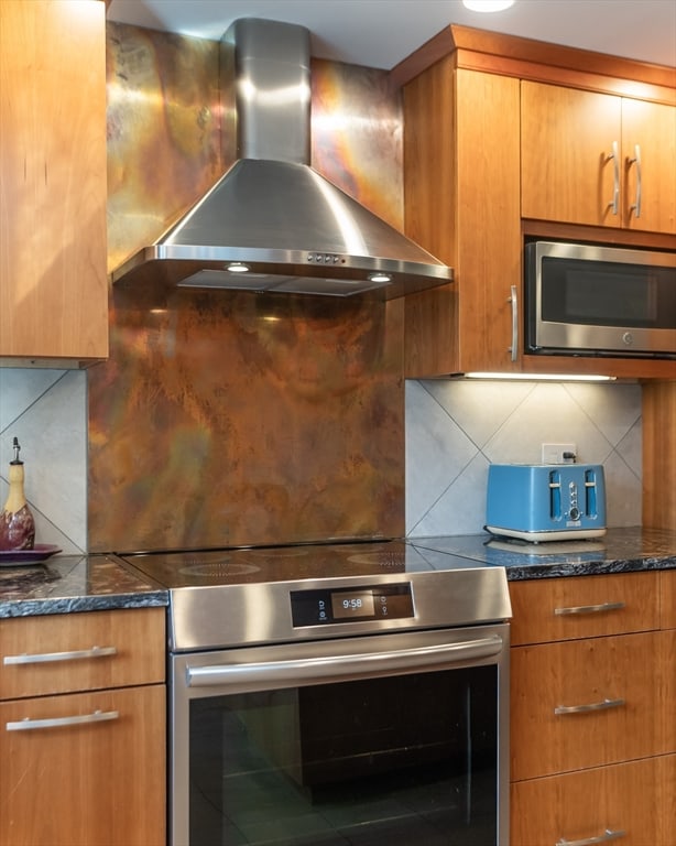 kitchen featuring appliances with stainless steel finishes, dark stone countertops, decorative backsplash, and wall chimney exhaust hood