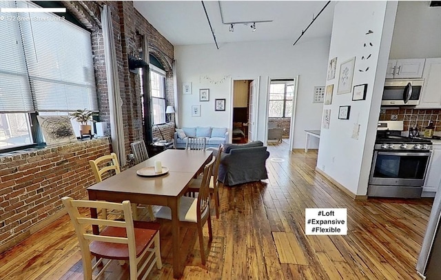 dining area featuring brick wall, rail lighting, and light wood-style flooring
