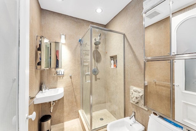 bathroom featuring visible vents, a sink, a shower stall, and tile walls
