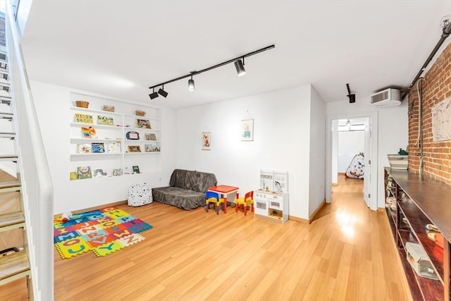 game room with rail lighting, a wall mounted AC, wood finished floors, and brick wall