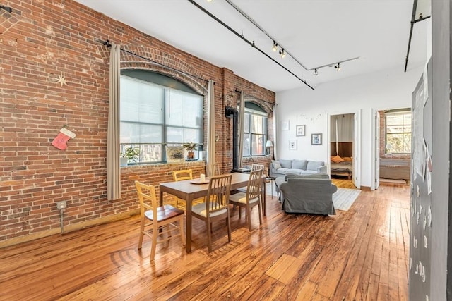 dining area featuring wood-type flooring, brick wall, track lighting, and a wealth of natural light