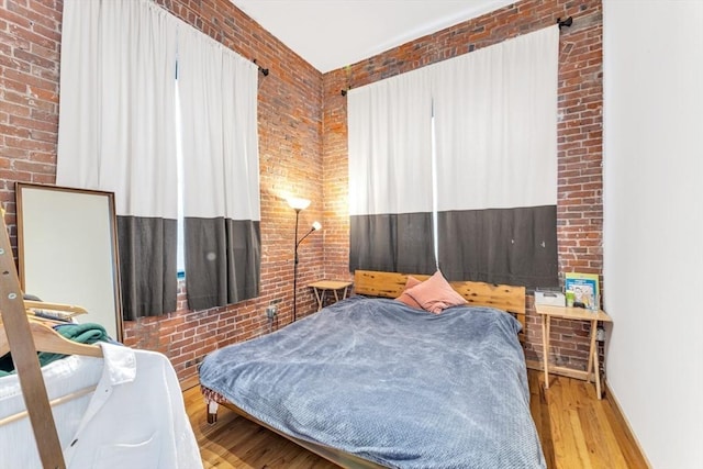 bedroom with wood finished floors and brick wall