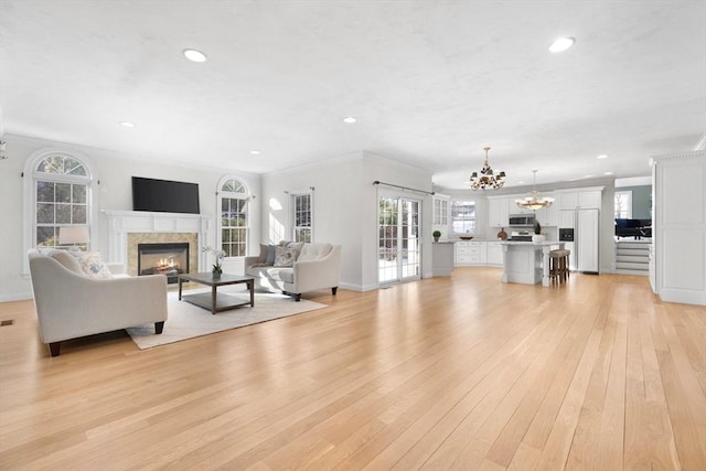 living room featuring a tile fireplace, ornamental molding, a chandelier, and light wood-type flooring