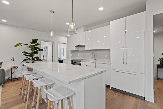 kitchen with white cabinetry, stainless steel range with electric stovetop, a kitchen island, sink, and pendant lighting