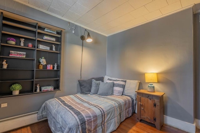 bedroom featuring ornamental molding, a baseboard heating unit, and hardwood / wood-style floors