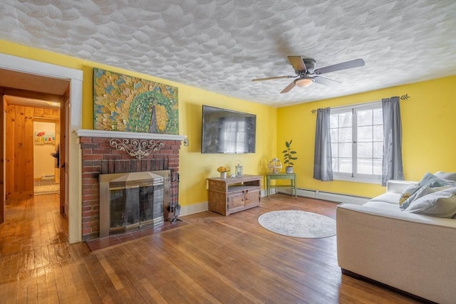 living room with a textured ceiling, baseboard heating, hardwood / wood-style flooring, ceiling fan, and a fireplace