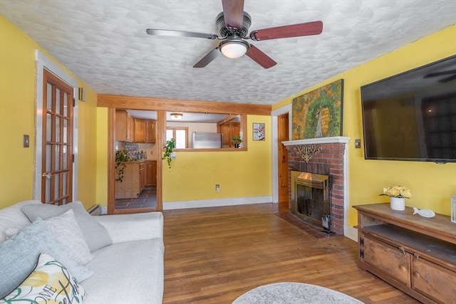 living room featuring ceiling fan, light hardwood / wood-style floors, a brick fireplace, and a textured ceiling