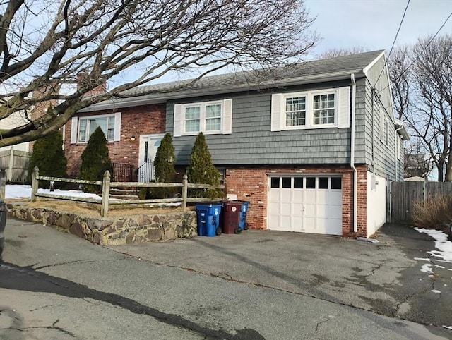 raised ranch featuring a fenced front yard, driveway, brick siding, and a garage