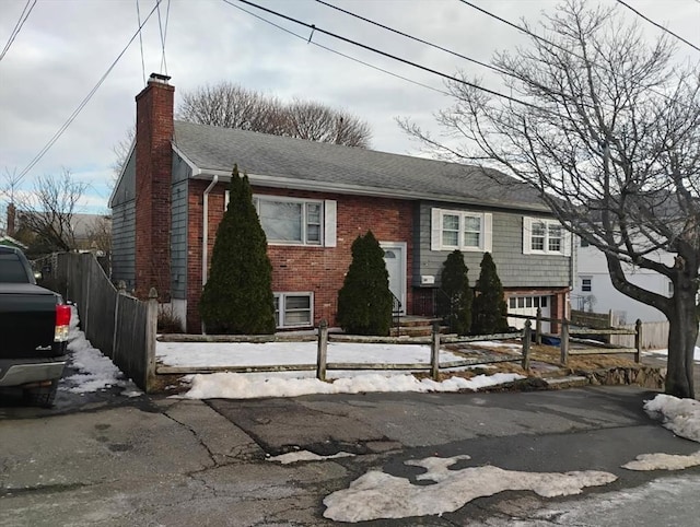 raised ranch with fence, brick siding, and a chimney
