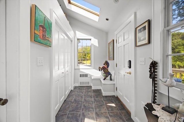 hall featuring lofted ceiling with skylight, radiator, dark tile patterned flooring, and plenty of natural light