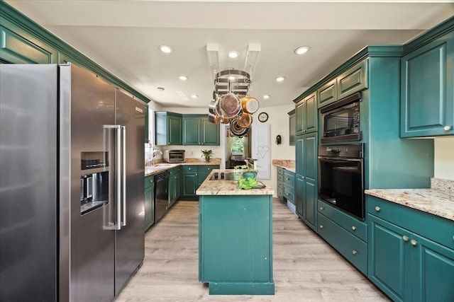 kitchen with light hardwood / wood-style flooring, black appliances, light stone counters, a kitchen island, and green cabinets