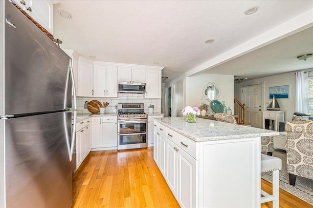 59 Brigantine Cir, Plymouth, MA 02360 - kitchen with appliances with stainless steel finishes, light wood-style floors, a kitchen island, a kitchen bar, and white cabinets