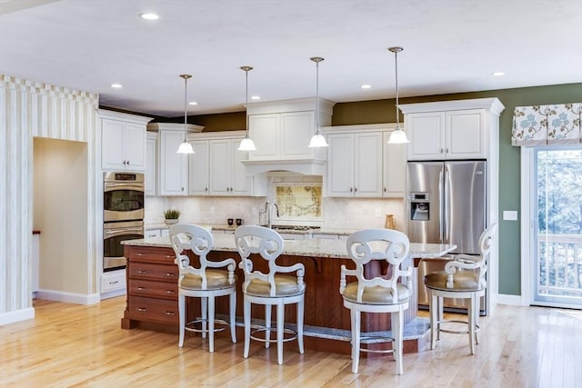 kitchen with appliances with stainless steel finishes, pendant lighting, a kitchen breakfast bar, light stone countertops, and a center island with sink