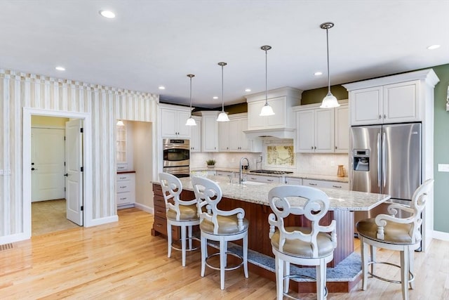 kitchen featuring appliances with stainless steel finishes, a center island with sink, a kitchen bar, and decorative light fixtures