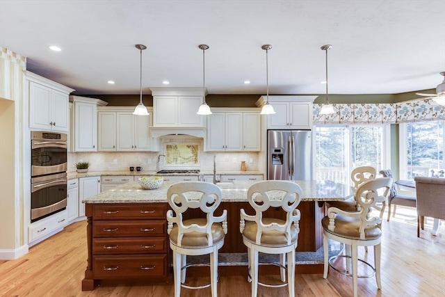 kitchen with hanging light fixtures, stainless steel appliances, white cabinets, and a center island with sink