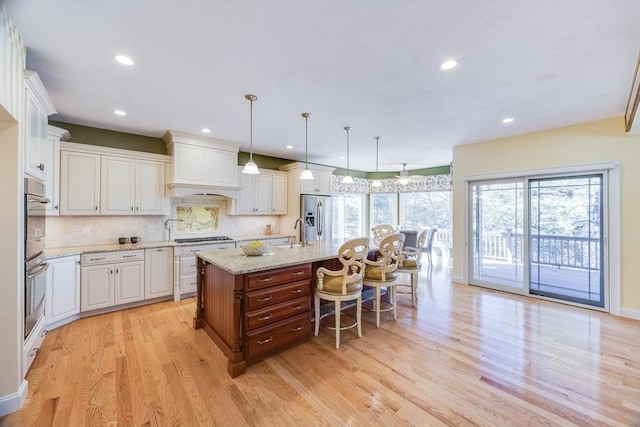 kitchen with a breakfast bar, decorative light fixtures, stainless steel appliances, light stone countertops, and a center island with sink