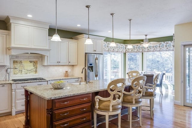 kitchen with white cabinetry, appliances with stainless steel finishes, a center island with sink, and decorative light fixtures