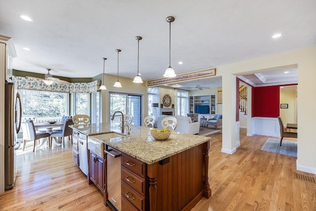 kitchen with sink, decorative light fixtures, light wood-type flooring, stainless steel fridge, and a kitchen island with sink