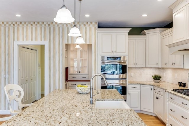 kitchen with pendant lighting, sink, light stone countertops, and double oven