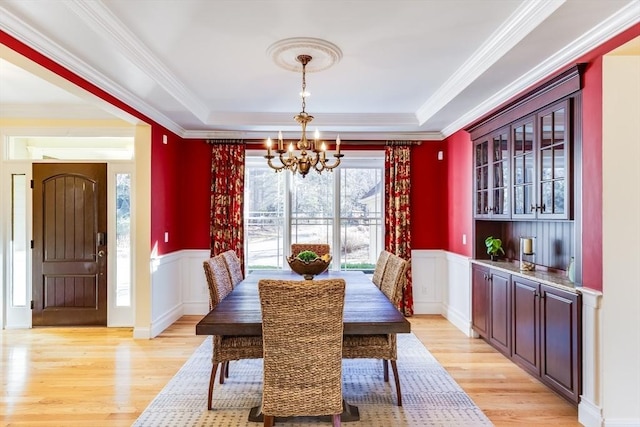 dining space with crown molding, a tray ceiling, light hardwood / wood-style floors, and a chandelier