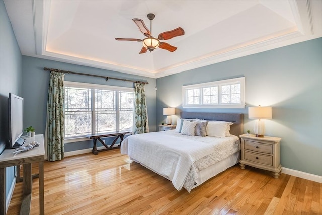 bedroom featuring a raised ceiling, ceiling fan, multiple windows, and light hardwood / wood-style floors