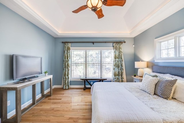 bedroom with ceiling fan, a tray ceiling, light hardwood / wood-style floors, and multiple windows