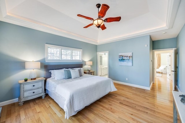 bedroom with ensuite bathroom, light hardwood / wood-style flooring, ceiling fan, and a tray ceiling