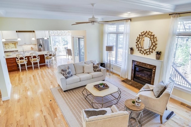 living room featuring crown molding, ceiling fan, a fireplace, and light hardwood / wood-style flooring