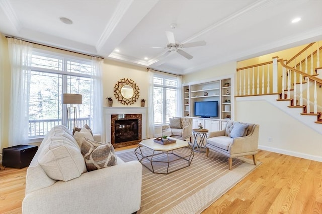 living room featuring crown molding, ceiling fan, a premium fireplace, and light hardwood / wood-style flooring