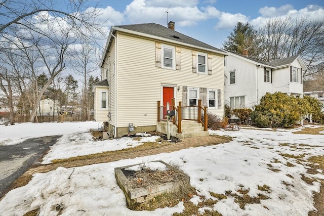 snow covered rear of property featuring a chimney