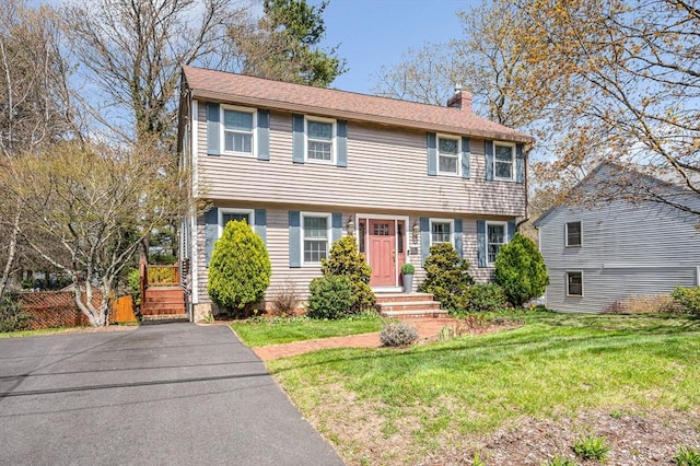 colonial home with a front lawn, fence, and a chimney