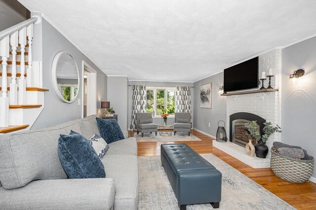 living area with baseboards, ornamental molding, a brick fireplace, wood finished floors, and stairway