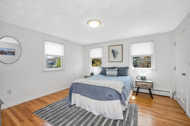 bedroom featuring light wood finished floors, baseboards, and a baseboard heating unit