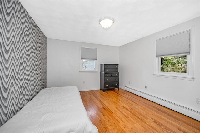 bedroom with light wood finished floors, baseboards, multiple windows, and a baseboard heating unit