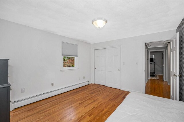 unfurnished bedroom featuring a baseboard heating unit, a closet, attic access, and wood finished floors