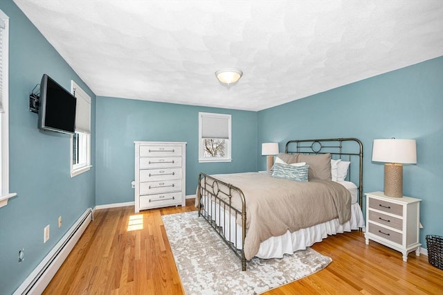 bedroom with light wood finished floors, baseboards, and a baseboard heating unit