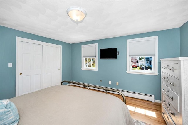 bedroom featuring a baseboard heating unit, a closet, multiple windows, and wood finished floors