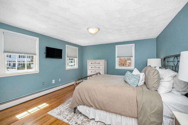 bedroom featuring a baseboard heating unit, multiple windows, and wood finished floors