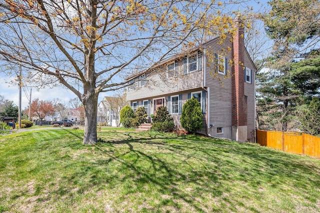 colonial-style house with a chimney, a front yard, and fence