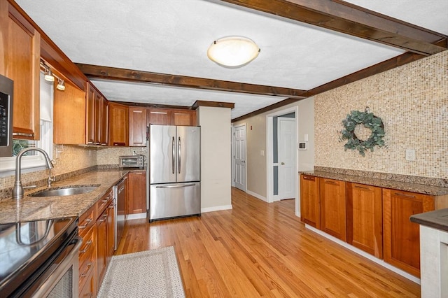 kitchen with a sink, light wood finished floors, decorative backsplash, and appliances with stainless steel finishes
