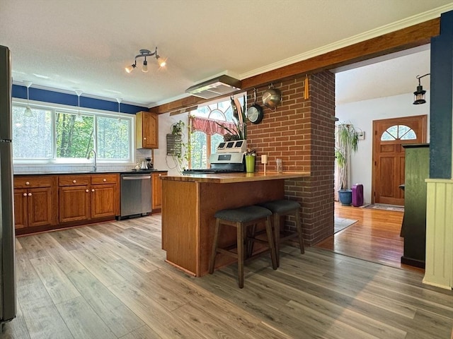 233 Old Wendell Rd, Northfield, MA 01360 - kitchen with appliances with stainless steel finishes, brown cabinetry, light wood-style floors, ornamental molding, and a kitchen breakfast bar