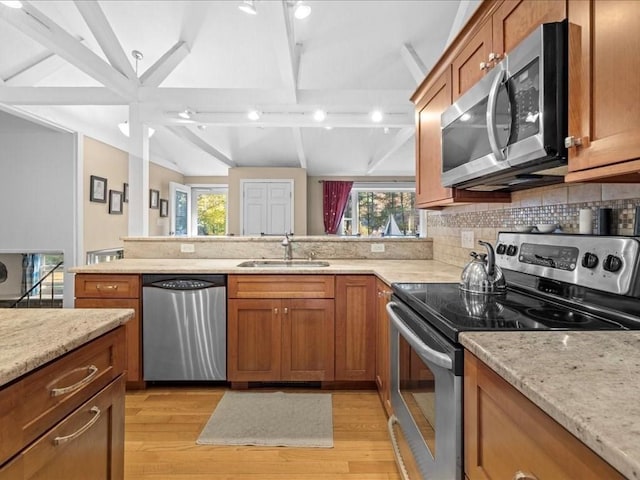 kitchen with brown cabinets, a sink, lofted ceiling with beams, stainless steel appliances, and light wood-style floors