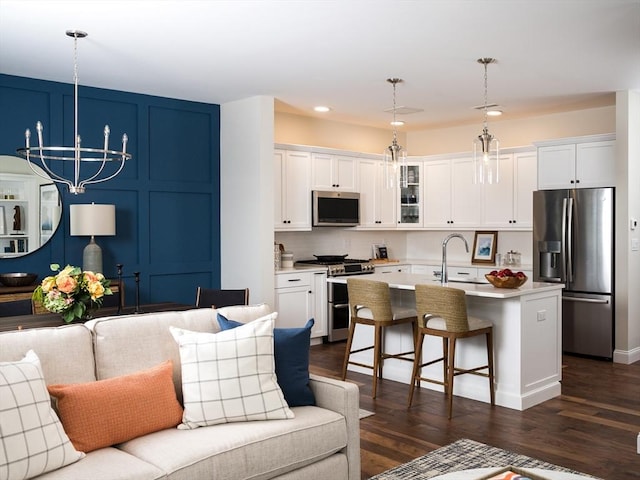 kitchen with sink, hanging light fixtures, a center island with sink, stainless steel appliances, and white cabinets