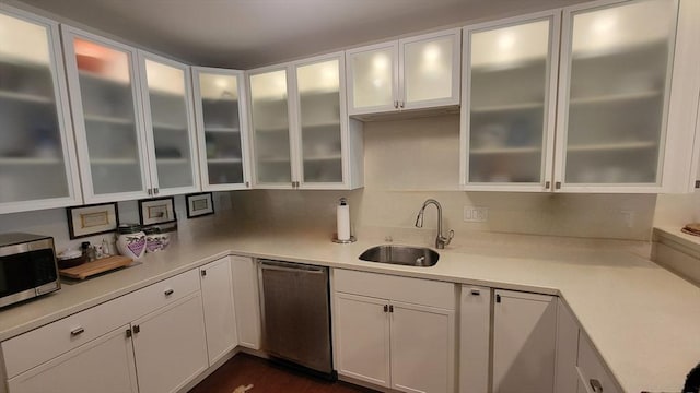 kitchen with appliances with stainless steel finishes, a sink, light countertops, white cabinetry, and glass insert cabinets