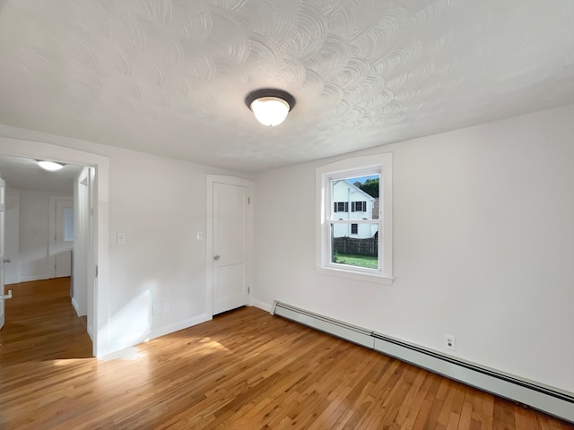 unfurnished room with baseboard heating, light hardwood / wood-style floors, and a textured ceiling