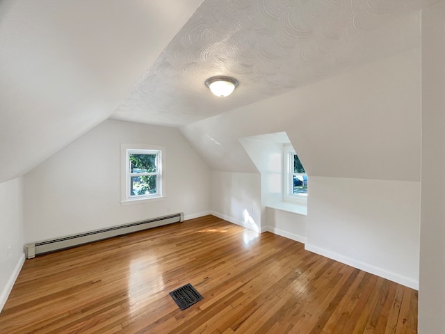 bonus room featuring a baseboard heating unit, vaulted ceiling, a textured ceiling, and wood-type flooring