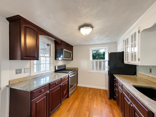 kitchen featuring a textured ceiling, light hardwood / wood-style flooring, light stone counters, and stainless steel appliances