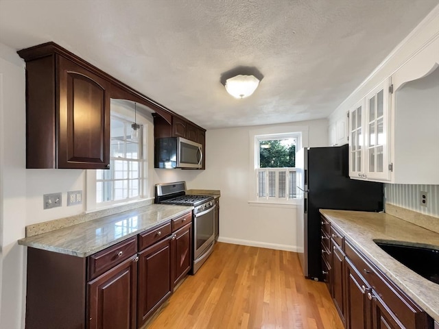 444 Lowell St, Reading, MA 01867 - kitchen with stainless steel appliances, light wood-style floors, baseboards, light stone countertops, and dark brown cabinetry